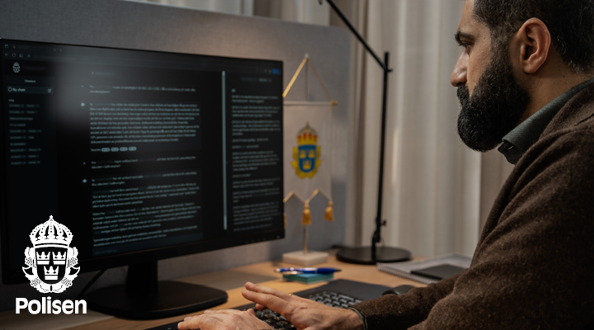 En man med skägg sitter framför en datorskärm. Polisens logotyp.