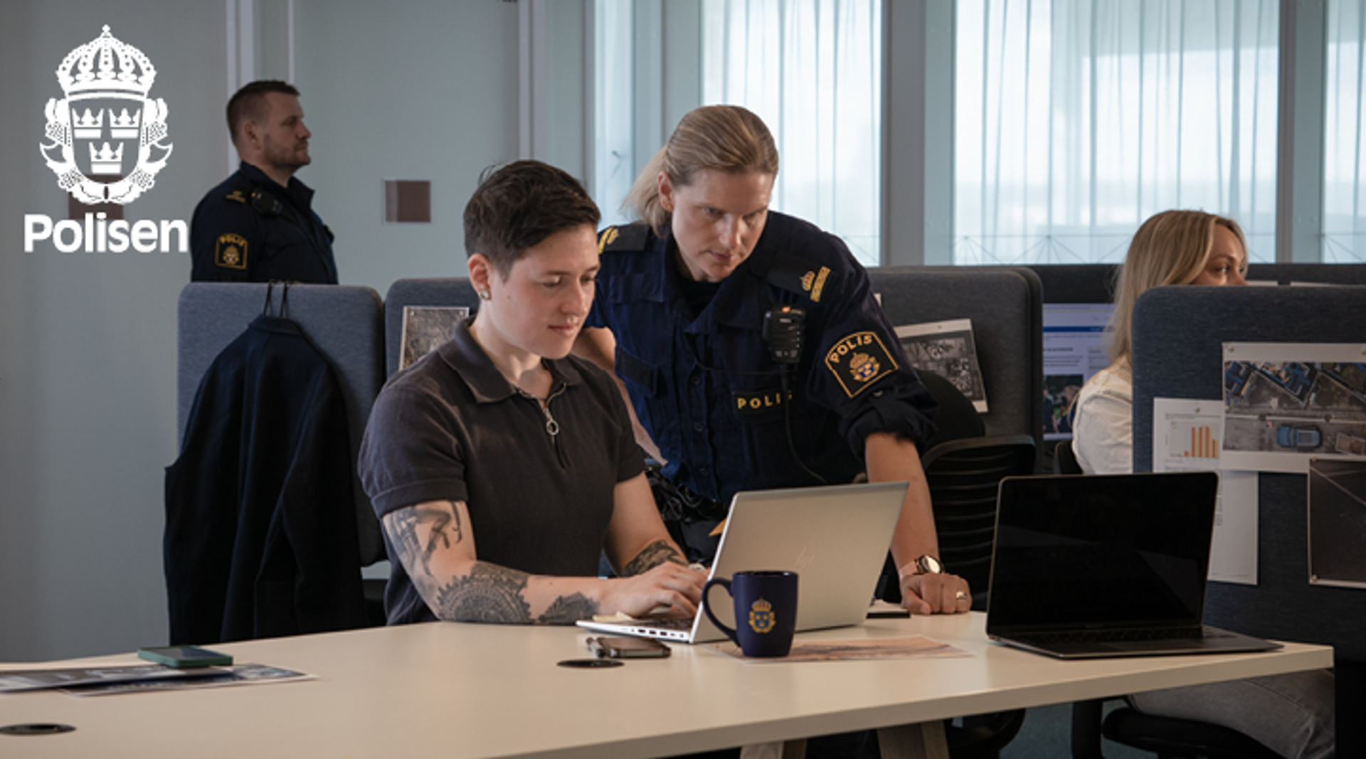 Poliser samtalar framför en datorskärm. Polisens logotyp.