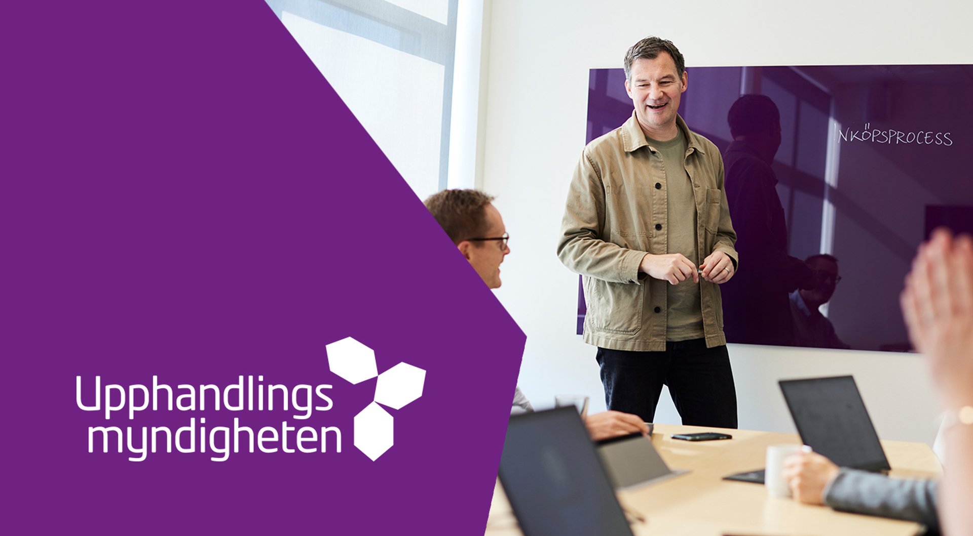 Glad man talar inför kollegor. Upphandlingsmyndighetens logotyp.