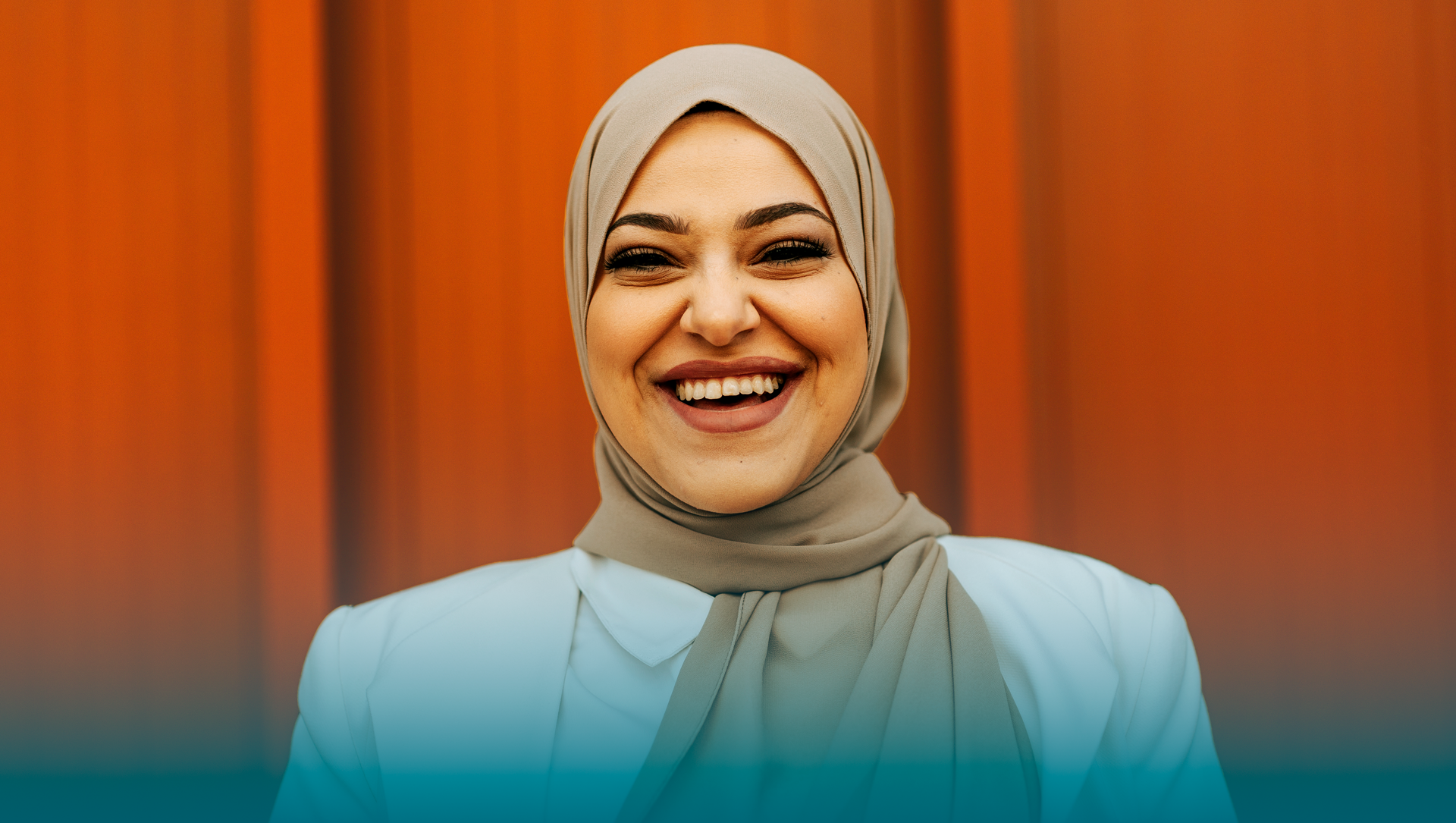 Glad kvinna i hijab framför rödmålad vägg.